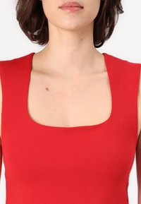Top sin mangas rojo con escote cuadrado, textura acanalada y silueta ajustada. Tela suave con un sutil tono de piel por debajo.