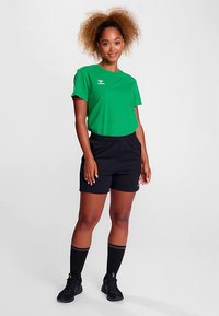 Zielona koszula z krótkim rękawem, czarne szorty z elastycznym pasem, podkolanówki. Codzienny strój sportowy odpowiedni do uprawiania sportu lub ćwiczeń.