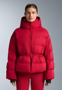 Piros steppelt dzseki magas gallérral és elasztikus derékrésszel, sima textúrával és nagy térfogatú ujjakkal a hőszigetelés érdekében.