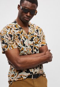 Μαύρο μπλουζάκι με κοντά μανίκια, διακοσμημένο με πολύχρωμα λουλουδάτα και παϊζάι μοτίβα, διαθέτει χαλαρό γιακά και μια μονόχρωμη μαύρη ζώνη. Υφασμάτινη υφή.