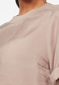 Camicia rosa chiaro a maniche corte realizzata in tessuto testurizzato, con scollatura rotonda e una leggera lucentezza, dal design morbido.