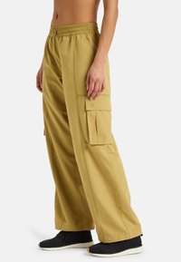Pantaloni cargo di colore khaki, dotati di una cintura elasticizzata, tasche laterali e una vestibilità comoda. Tessuto testurizzato con dettagli minimi.