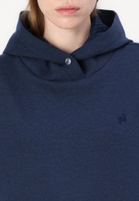 Felpa con cappuccio blu navy realizzata in morbido tessuto, con un chiusura a bottone al collo e un logo in rilievo discreto sul petto.