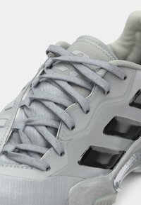 Lys grå sneakers med matchende snørebånd, polstret krave og sorte rektangulære designelementer på siden.