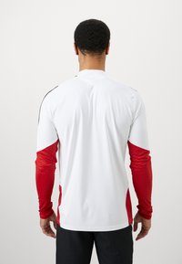 Ανδρική αθλητική μπλούζα με λευκό σώμα και κόκκινες υφασμάτινες μανσέτες. Διαθέτει στρογγυλή λαιμόκοψη και αντίθετες μαύρες ραφές στους ώμους.