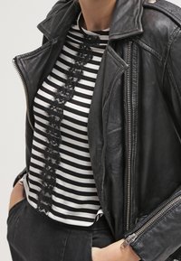 Černá kožená motorkářská bunda přes bílé a černé pruhované tričko s centrálním krajkovým detailem. Detailní pohled, zaměřený na textury a vzory.