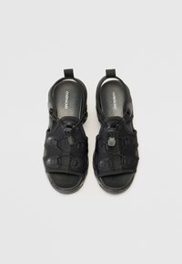 Black sandals with a textured rubber sole, adjustable straps, and a quick-release buckle. Open-toe design with reinforced accents.