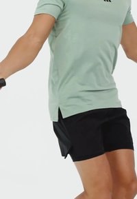 Camisa verde claro de manga corta con aberturas laterales, combinada con pantalones cortos negros, ambos hechos de tela transpirable para ropa deportiva.