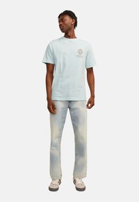 Tricou din bumbac de culoare albastru deschis, cu mâneci scurte și guler rotund, având un logo grafic pe piept; asortat cu blugi de denim deschis.