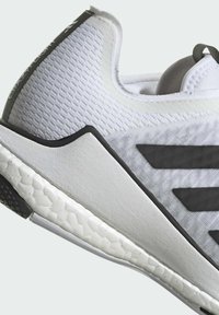 Weißer Sportschuh mit strukturiertem Obermaterial, schwarzen Akzenten und einer gemusterten Gummisohle. Verfügt über eine abgerundete Ferse und minimales Branding.
