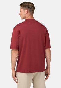 Bordeauxrotes T-Shirt mit kurzen Ärmeln, Rundhalsausschnitt, glatter Textur und lockerem Schnitt, kombiniert mit hellbeigen Hosen.