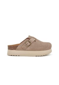 Zoccoli in camoscio beige con una suola in sughero robusta e texturizzata, dotati di una fibbia e punta arrotondata. Design piatto con un leggero rialzo nel tallone.