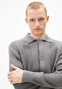 Polo-shirt gris à côtes avec un col, comportant deux boutonnières. Le tissu semble doux et texturé, épousant étroitement les épaules.