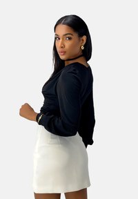 Zwarte top met lange mouwen en plooien, gecombineerd met een witte rok met hoge taille. Gouden armband en oorbellen zorgen voor metallic accenten.