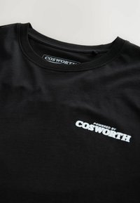Camiseta negra de cuello redondo con el texto blanco "Powered by COSWORTH" impreso en el pecho cerca del cuello.