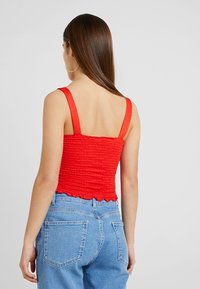 Top corto rojo con bordado, tirantes anchos y dobladillo en forma de ondas, combinado con jeans de cintura alta en azul claro que tienen bolsillos traseros.