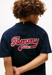 Marineblå kortærmet t-shirt lavet af bomuld, med et stort rødt og hvidt "Tommy" logo og "CLASS OF 1985" på ryggen.