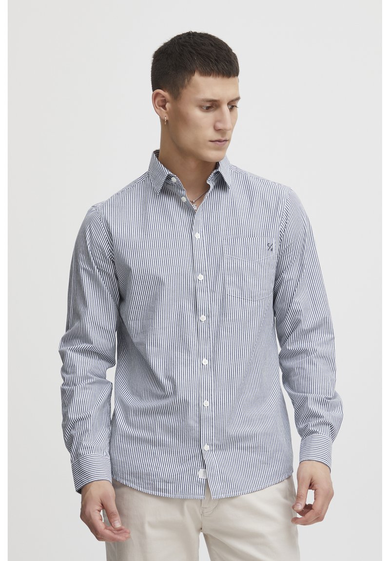 Camicia a righe con bottoni, con sottili righe blu navy e bianche, maniche lunghe, taschino singolo sul petto e colletto classico. Tessuto di cotone.