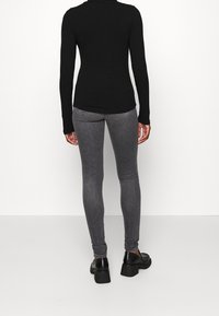 Top de manga larga negro de canalé combinado con jeans ajustados gris claro. El conjunto se completa con zapatos de plataforma negros. Diseño sencillo y ajustado.