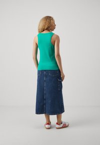 Turquoise ribbed tank top with a round neckline paired with a long blue denim skirt featuring pockets and a straight cut. White sneakers with red accents.