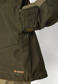 Olivenfarget G-1000-stoffjakke med mansjetter med borrelås og sidesøm med blå og gul detalj.