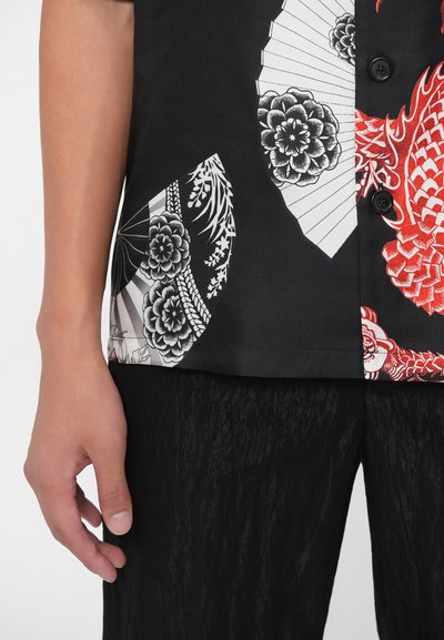 Camicia a maniche corte in tessuto nero con motivo floreale e a ventaglio rosso e bianco, con chiusura a bottone e texture liscia.