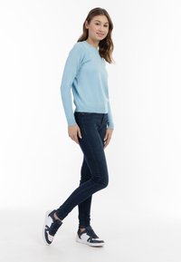 Maglione azzurro chiaro a maniche lunghe con orlo a coste, abbinato a jeans skinny blu scuro e sneaker navy con accenti bianchi.