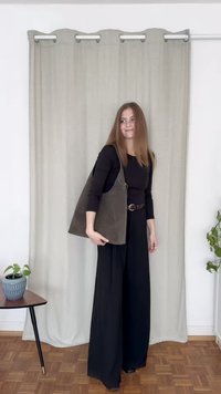 Suede shoulder bag in dark gray with a minimalist design, featuring a curved shape and open top. Model wears black top and wide pants.