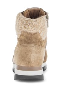 Tan suède enkellaarsjes met een fuzzy tan kraag, achterrits en een zwarte rubberen zool met een witte tussenzoolrand.