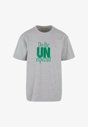 T-shirt en coton gris avec un col rond et des manches courtes, portant le texte "Faites comme attendu par l'ONU" en vert.