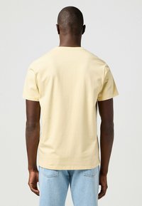 Camiseta amarilla de manga corta hecha de algodón suave, con cuello redondo y un corte relajado. La vista trasera muestra una textura suave y un diseño sencillo.