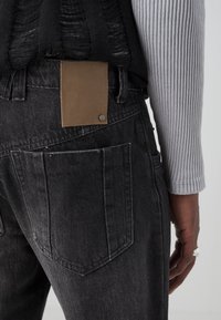 Svarta denimjeans med en brun läderlapp på baksidan av midjebandet. Innehåller en texturerad, vävd svart topp och en ruggad grå långärmad tröja.