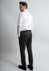 Witte lange mouwen shirt, donkergrijze broek en zwarte schoenen. Het shirt heeft een klassieke kraag; de broek heeft achterzakken en een slim fit.