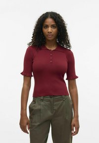 Burgundské polo tričko s ribkováním a krátkými volánovými rukávy, se čtyřmi knoflíky na zapínání. Kombinované s olivově zelenými kalhotami s rovnou přední stranou.
