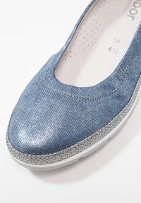 Ballet flats en denim bleu avec une finition métallique texturée, un bout rond et un accent pailleté argent le long de la semelle.