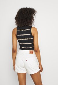 Body noir tie-dye avec des rayures beige, associé à un short en denim blanc avec un patch logo visible et des ourlets retroussés.