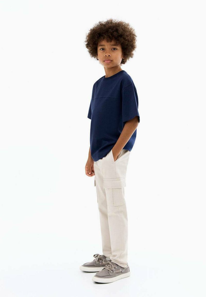 Marineblauw T-shirt met korte mouwen met een vlakke naadontwerp, beige cargobroek met meerdere zakken, grijze sneakers met witte zolen.