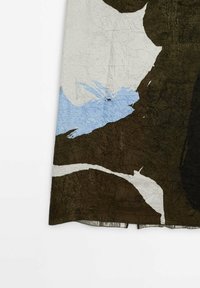 Tissu marron avec de grandes formes abstraites blanches et bleues, montrant une texture froissée et un ourlet légèrement évasé sur un fond uni.