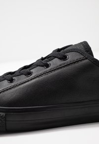 Baskets en cuir noir avec lacets noirs et coutures, présentées en gros plan sur fond blanc.