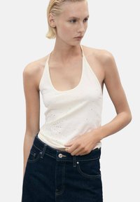 Top in cotone bianco a halter con scollo rotondo, impreziosito da piccole pietre strass, abbinato a jeans in denim scuri a vita alta.