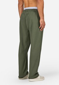 Zelené prúžkované voľné nohavice s elastickým pásom, širokým strihom a mäkkou textúrou; nosené s bielymi teniskami. Pohľad zozadu.