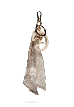 Sciarpa di seta beige con motivo, attaccata a un portachiavi dorato con ciondoli color crema di forma circolare e astratta.