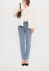 Jasno beżowa kurtka z guzikami noszona na białym topie na ramiączkach, w połączeniu z niebieskimi dżinsami z wysokim stanem i czarnymi butami na szpilkach. Prosty design i kolory.