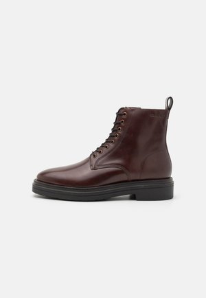 Brown leather ankle boots with round toe, seven eyelet lace-up front, and a black rubber sole. Features a pull tab at the heel.