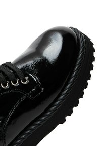 Chaussure en cuir verni noir avec un bout rond, un laçage, œillets métalliques et semelle en caoutchouc noir dotée d'un motif de tread texturé.
