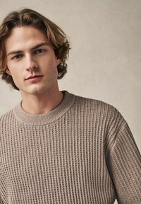 Jersey de punto beige con un diseño de canalé texturizado y un escote redondo, que cuenta con mangas largas y un corte relajado.