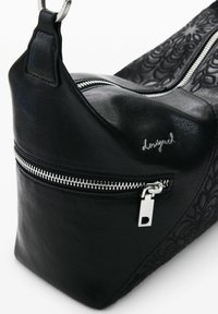 Must nahast õlakott hõbedaste lukkudega taskutega, külgedel reljeefne lillemuster ja väike metallist logo detail.