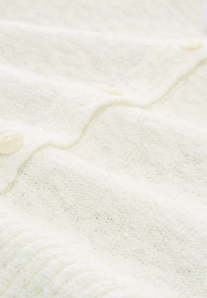 Tessuto lavorato a maglia di colore crema con bordo a coste e bottoni traslucidi, che mostra una parte del davanti abbottonato di un indumento.