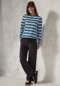 Camicia a maniche lunghe a righe blu, abbinata a pantaloni neri con coulisse. Il modello indossa sneakers nere con lacci bianchi. Tessuto morbido, vestibilità rilassata.