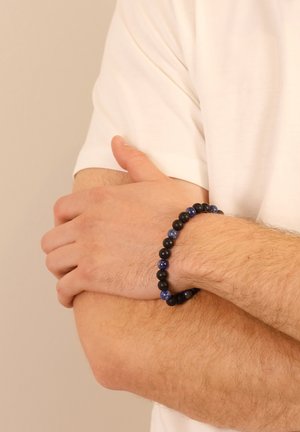 Beaded bracelet featuring black and dark blue stones, alternating in a circular pattern, worn on a wrist against a light background.